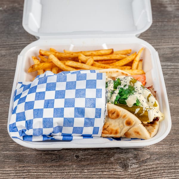 Tony's Gyros Greek Cuisine gyro with fries in a white takeout container on a wooden table.