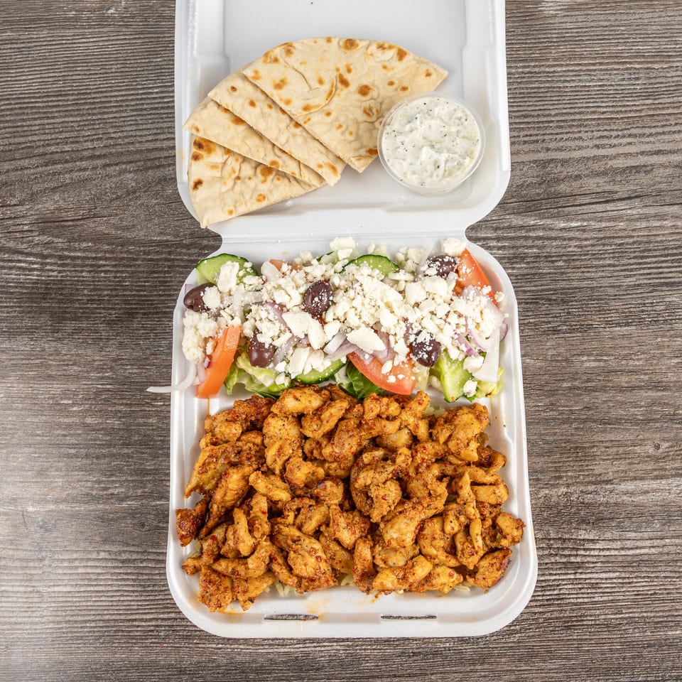 Tony's Gyros Greek chicken entree with Greek salad, pita bread, and tzatziki sauce in a takeout container.